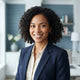 A diverse woman with a friendly, confident expression posing for a professional headshot in a bright, modern interior.